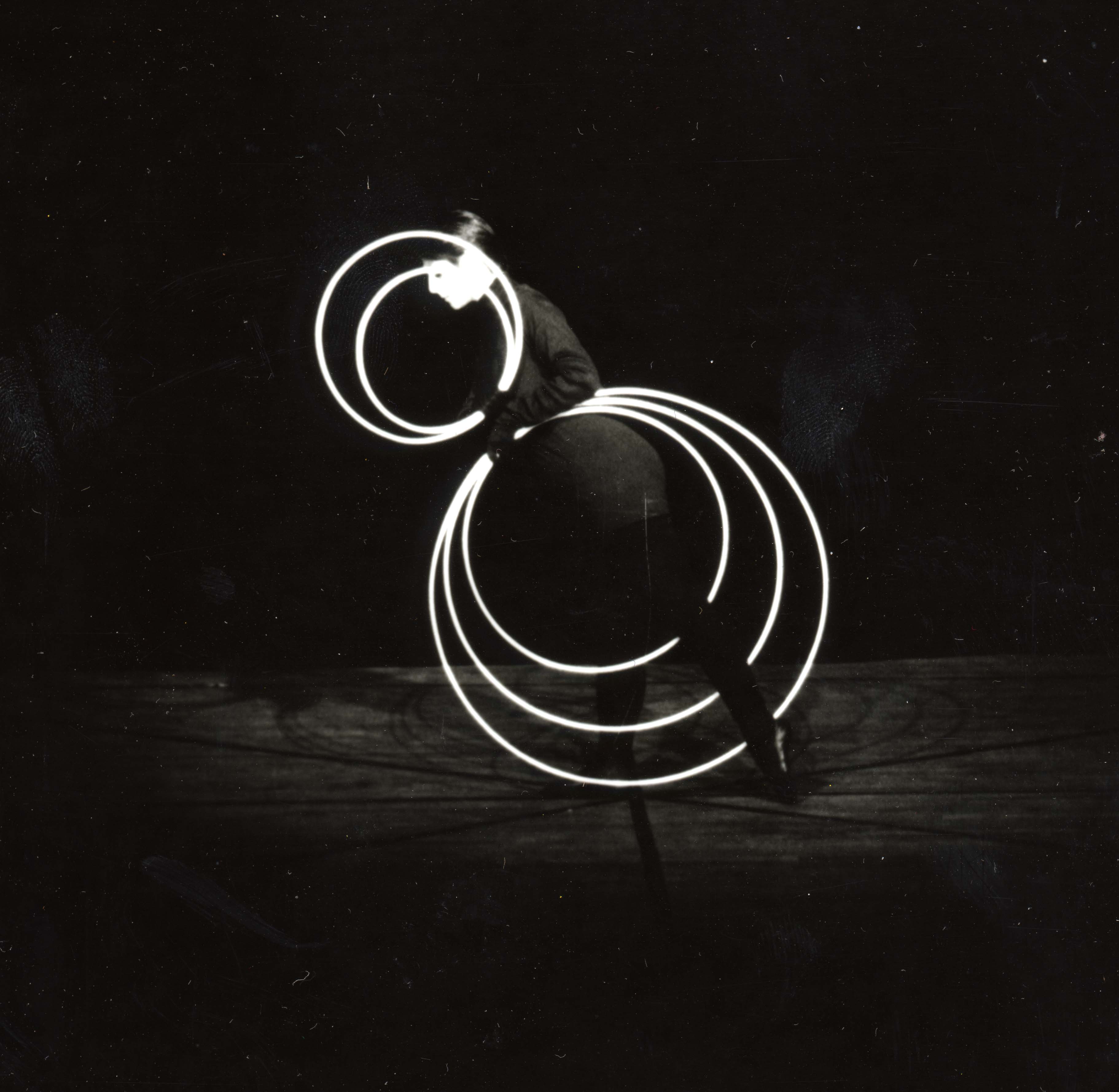 Reinfentanz performance. A dancer stands on one foot with her left foot stretched back, holding five white rings. Two rings form concentric circles near her head, three form concentric circles below her hips.